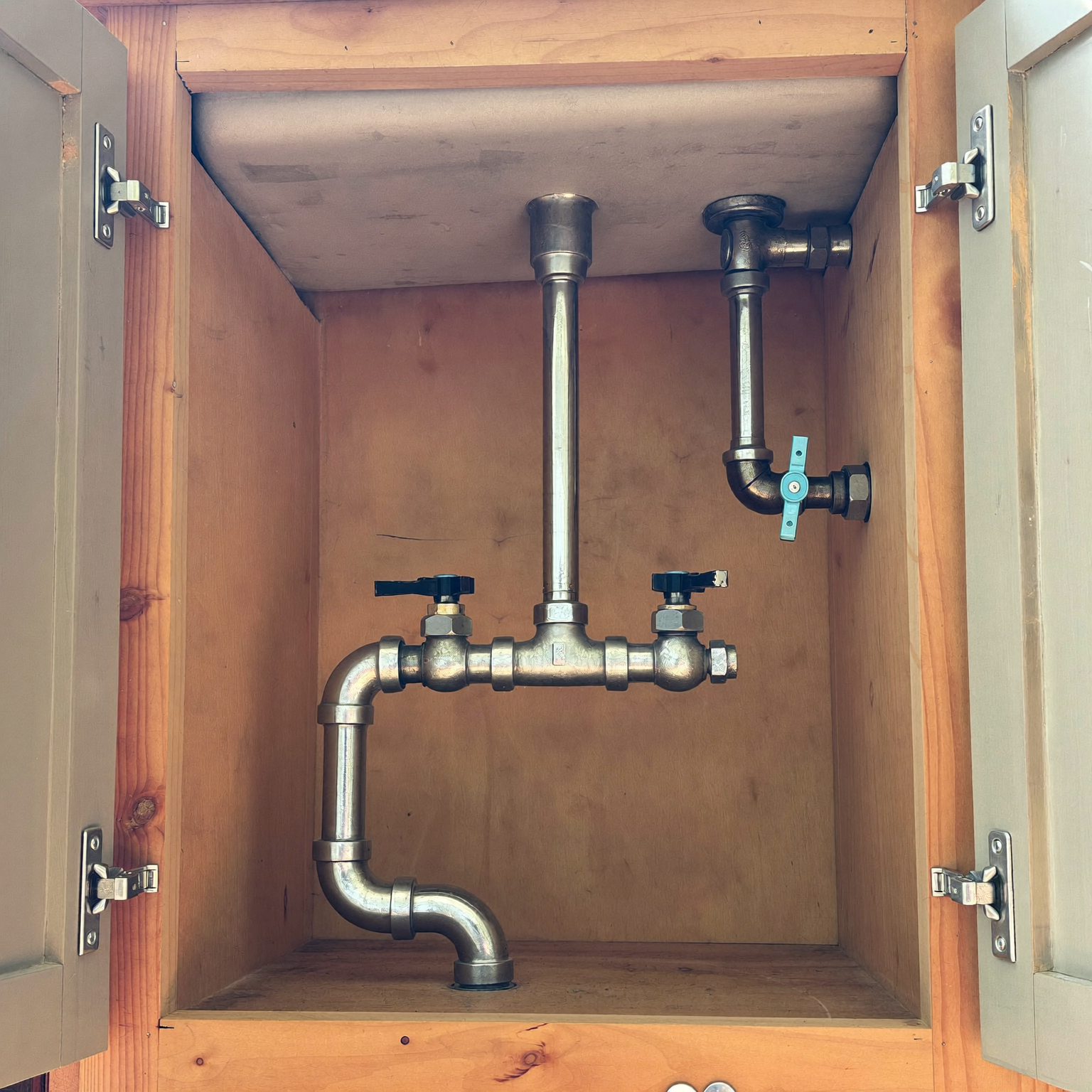 Exposed sink drain trap and shutoff valves inside an open kitchen cabinet during a plumbing inspection.